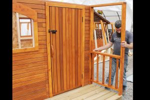 13. Align a porch rail in an upright position on the porch frame and attach it to the front wall and to the porch frame with screws.